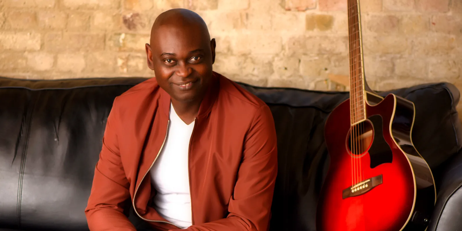 Yemi Alafifuni on the studio sofa with his guitar, photographed in 2020