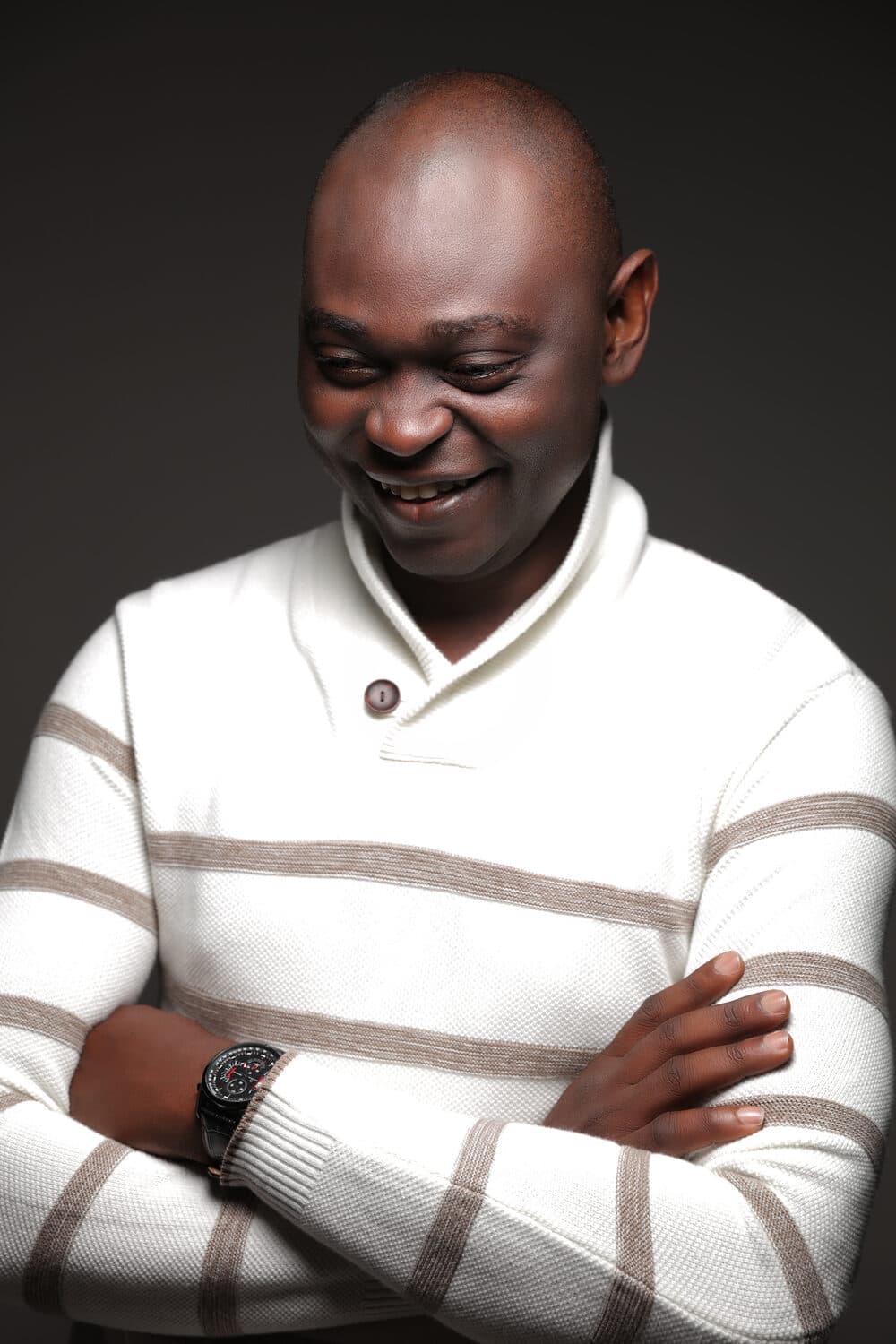 Yemi Alafifuni, head lowered, laughing, lit from one side against a dark ground