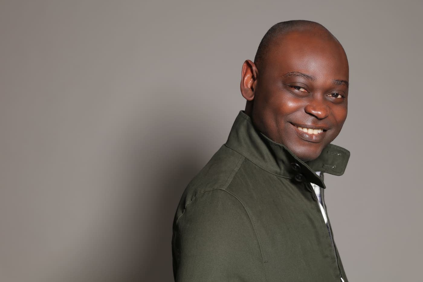 Yemi Alafifuni in an olive jacket against a warm grey ground