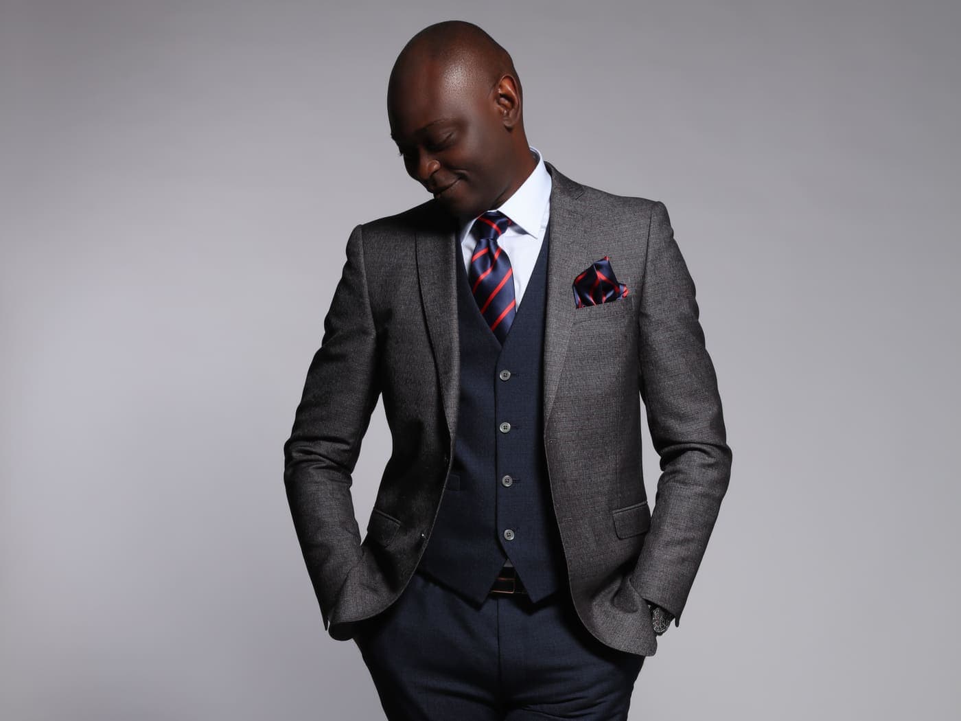 Yemi Alafifuni in a three-piece suit, head bowed, grey seamless backdrop