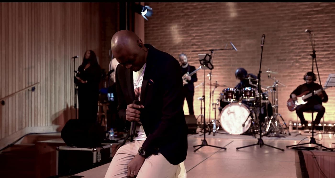 Yemi Alafifuni on stage with his band, head bowed over the microphone, at Canterbury Cathedral Lodge